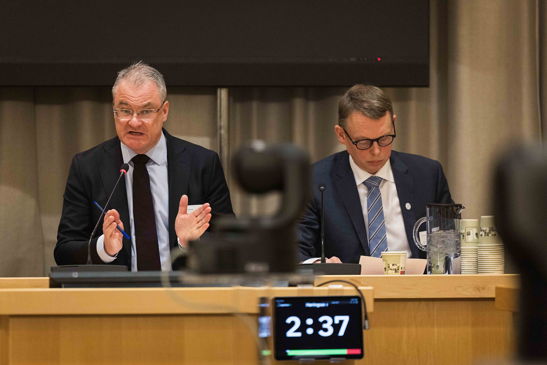 Et par menn som sitter ved et bord med mikrofoner