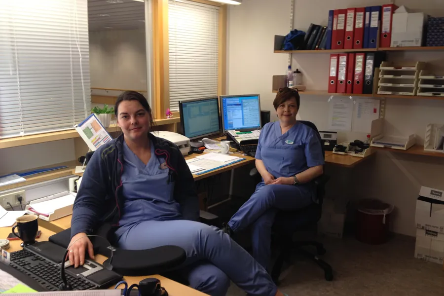 Et par kvinner som sitter ved et skrivebord med datamaskiner