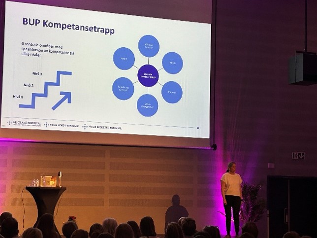 En person som står på en scene foran en stor skjerm