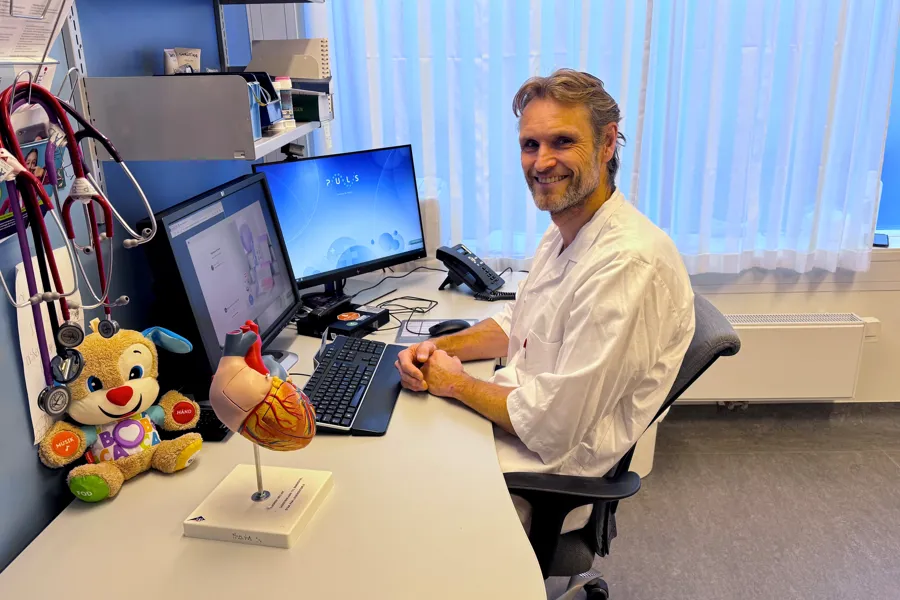 En mann som sitter ved et skrivebord med en datamaskin og et kosedyr