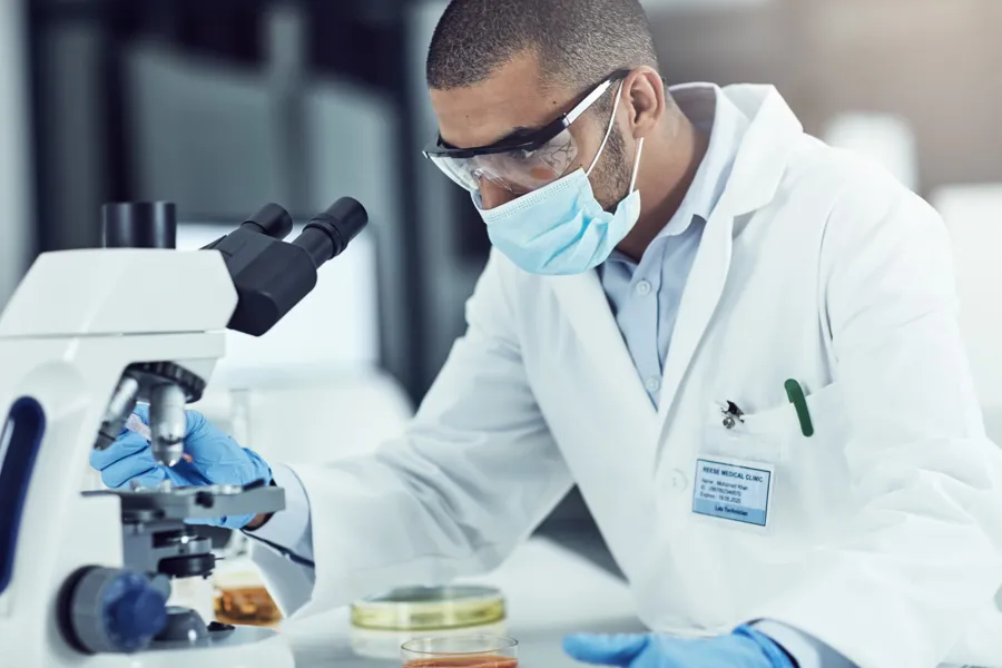 En mann i laboratoriefrakk som ser gjennom et mikroskop