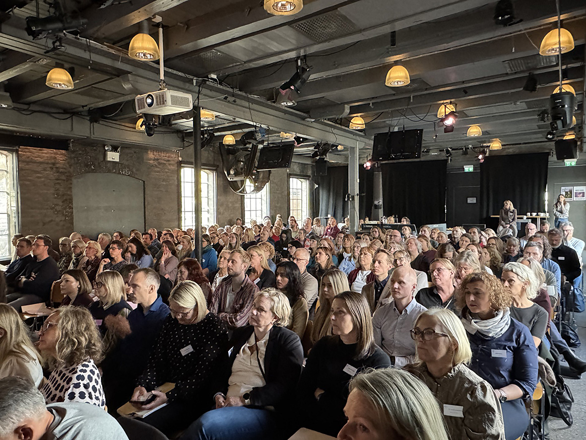 En stor mengde mennesker i et rom med en scene og en person på en scene