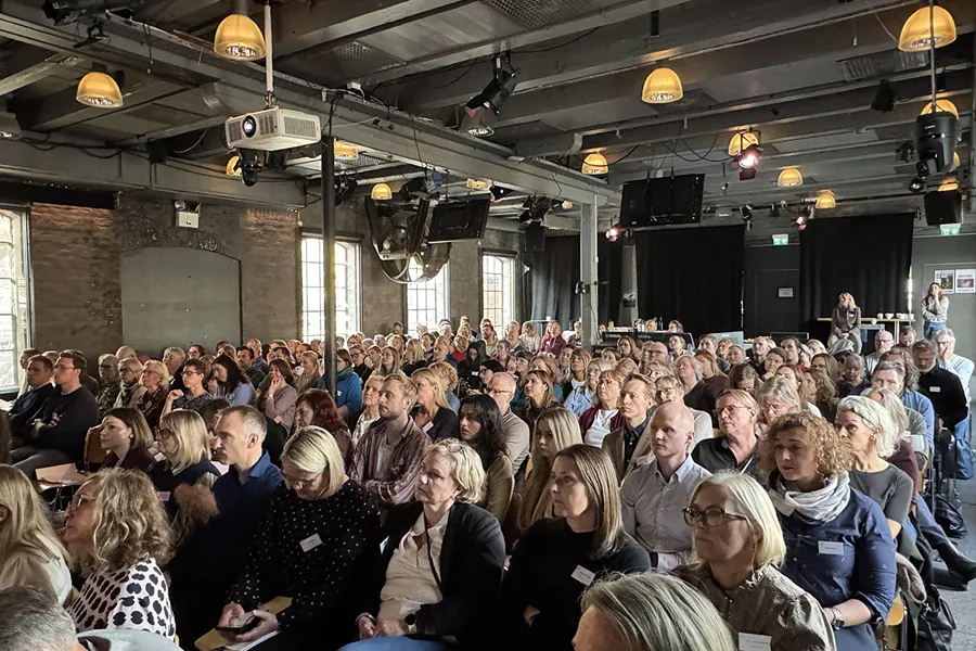 En stor mengde mennesker i et rom med en scene og en person på en scene