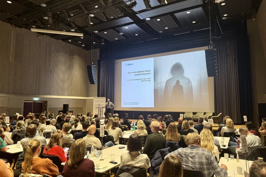 En gruppe mennesker som sitter i et rom med en stor skjerm