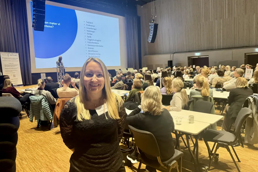 En kvinne som står foran en gruppe mennesker som sitter ved bordene