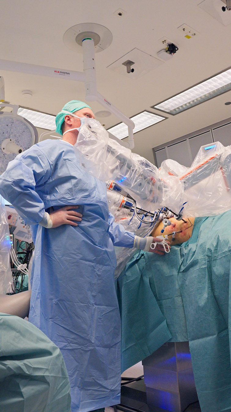 En person i kirurgisk uniform som holder en baby i en sykehusseng