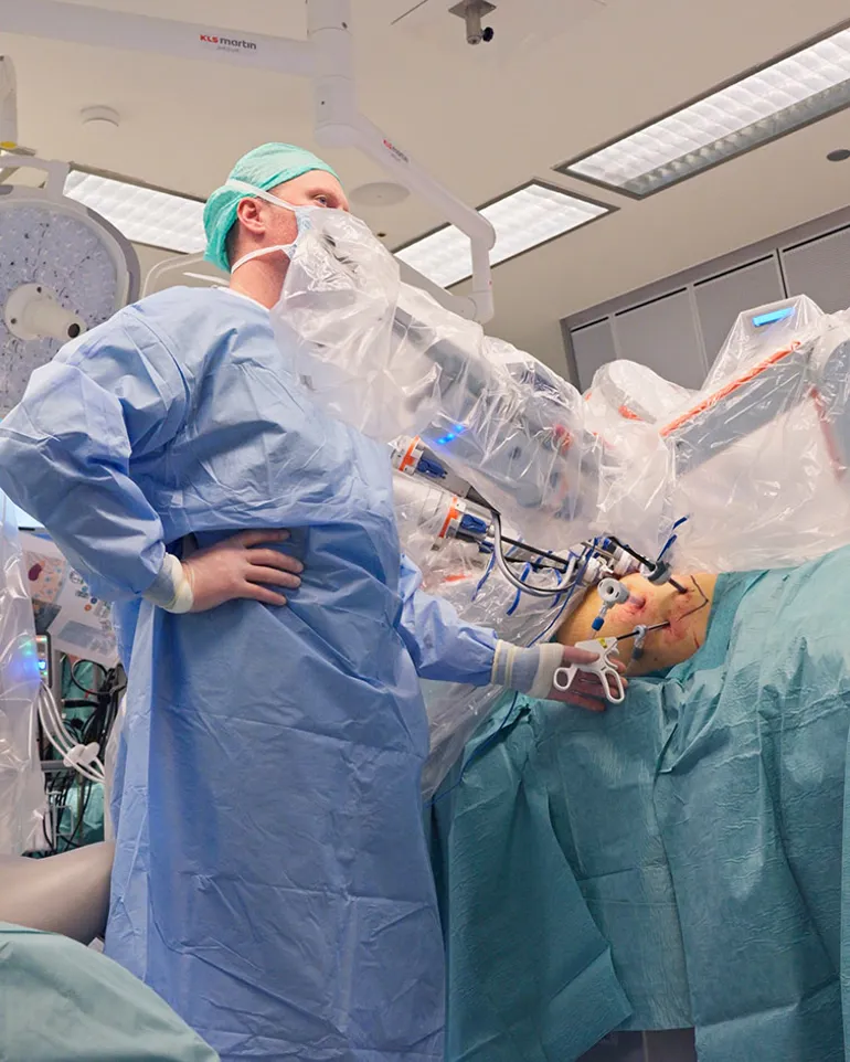 En person i kirurgisk uniform som holder en baby i en sykehusseng