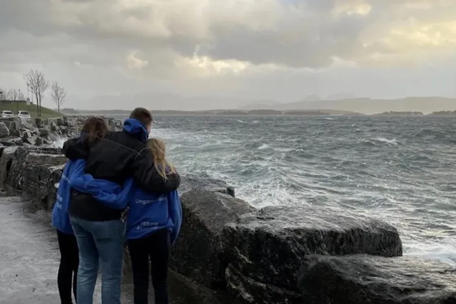 En gruppe mennesker som står på en steinete strand og ser på havet